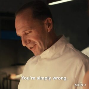 A still from the movie The Menu; Ralph Fiennes as The Chef, smiling and looking down from the camera with text that reads: You're simply wrong.
