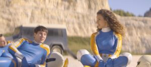 A man and a woman in yellow and blue Super Sentai style suits sit chatting.