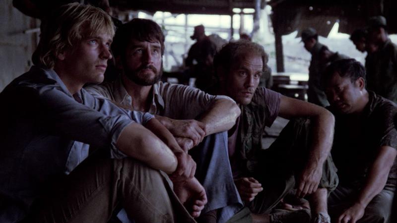 Actors Julian Sands and John Malkovich sit with scenemates in a still from the movie The Killing Fields